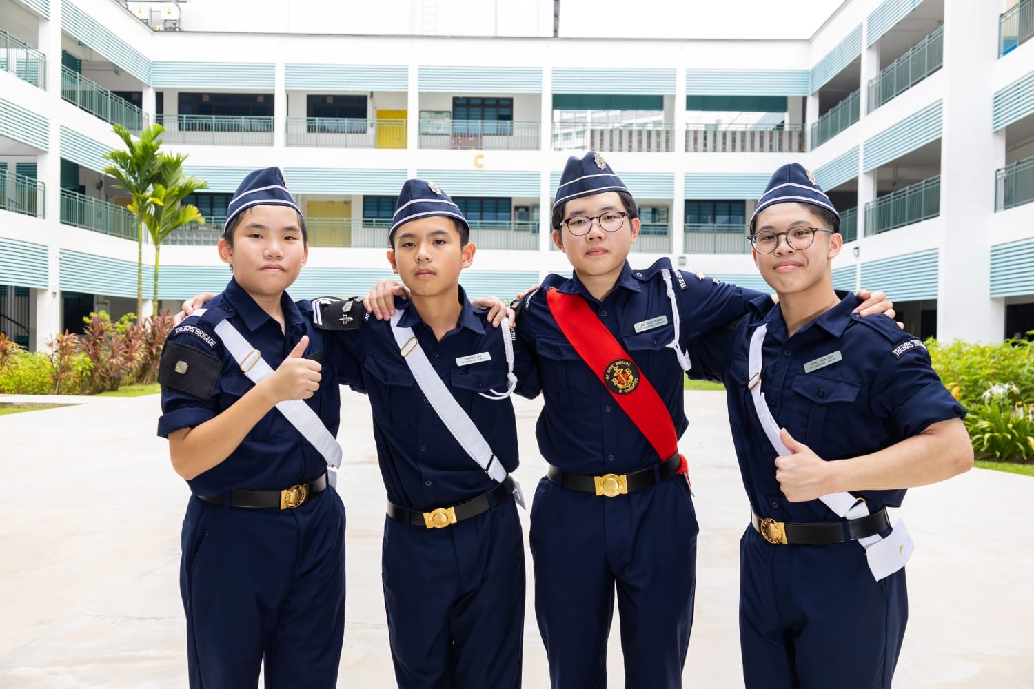 A group of 4 boys in boys brigade uniform with arms crossing each others' shoulders posing for a photo